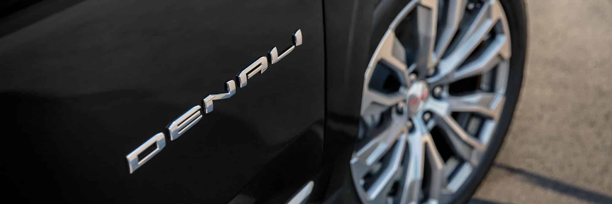 Close-up of a black vehicle with "Denali" badge and stylish alloy wheel.