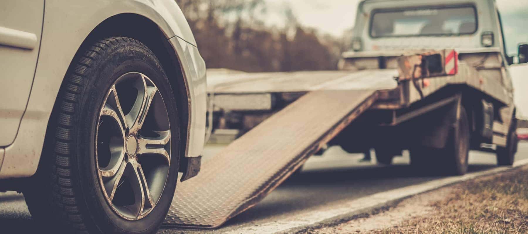 Car being loaded onto a tow truck ramp on the roadside.