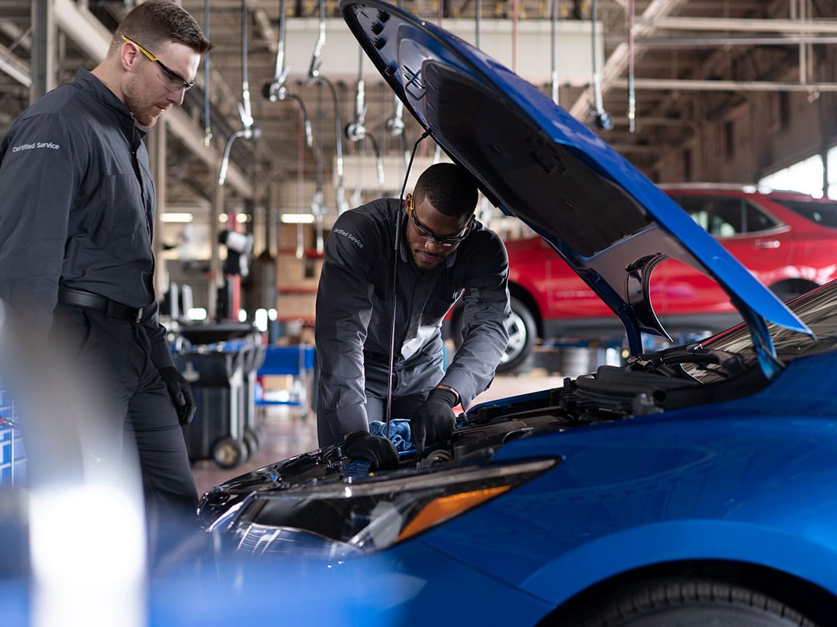 Two mechanics inspecting a blue car's engine in an auto repair shop.