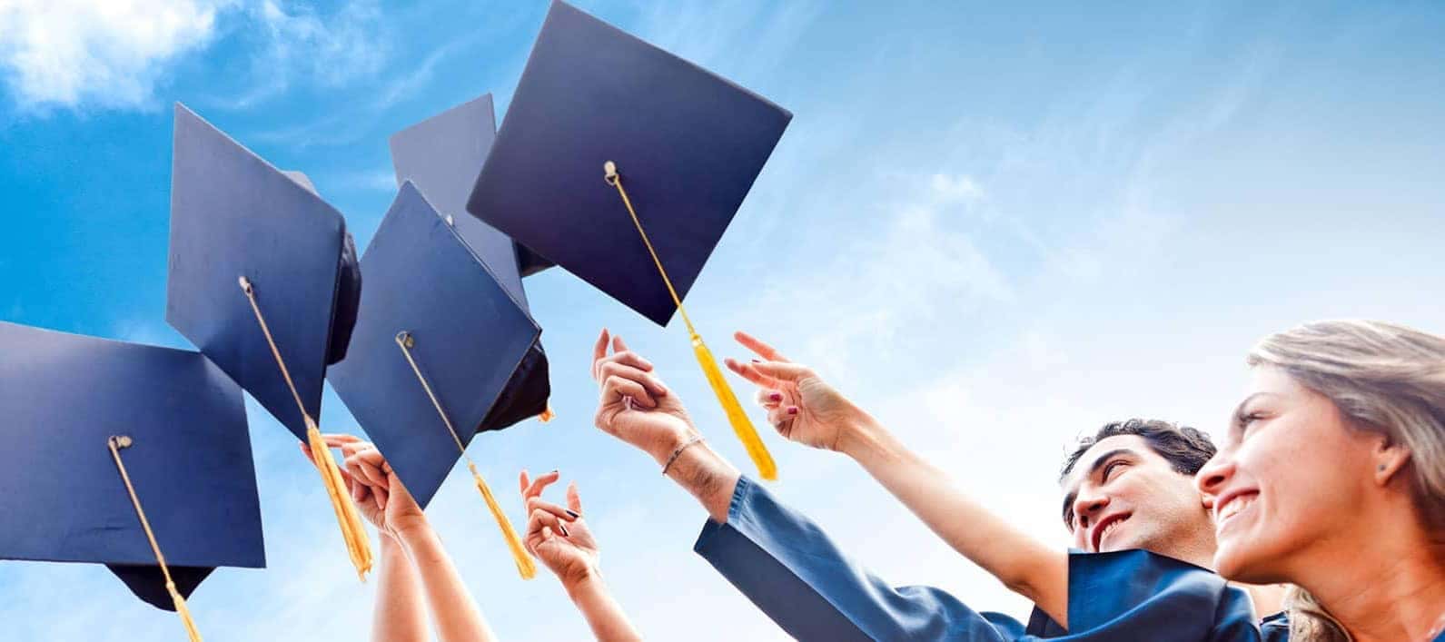 Graduates joyfully toss caps in the air against a clear blue sky, symbolizing achievement and celebration.