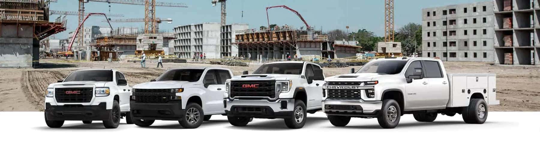 Four GMC and Chevrolet trucks parked at a construction site with cranes and buildings in the background.
