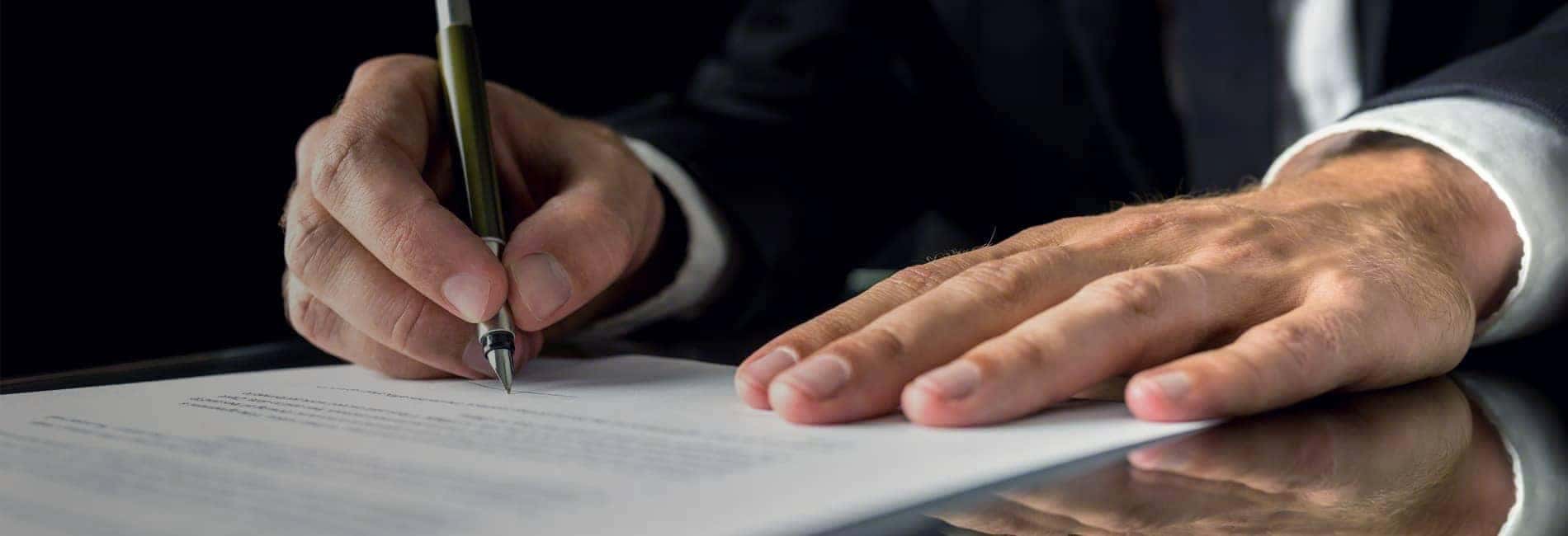 Close-up of a hand signing a document with a pen, suggesting a business or legal context.