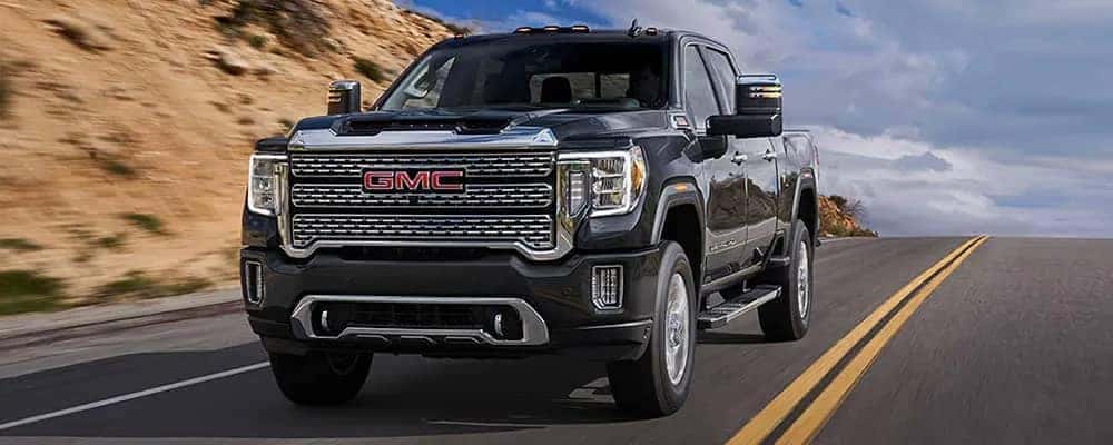 Black GMC pickup truck driving on a highway with a rocky landscape in the background.