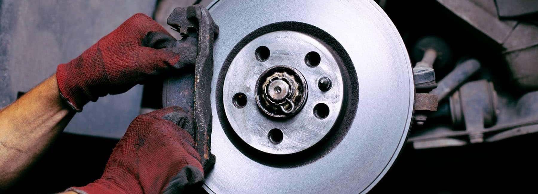 Mechanic with red gloves working on a car's brake disc system repair.