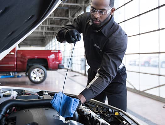 Mechanic checking engine oil level in a car workshop with a red truck in the background.