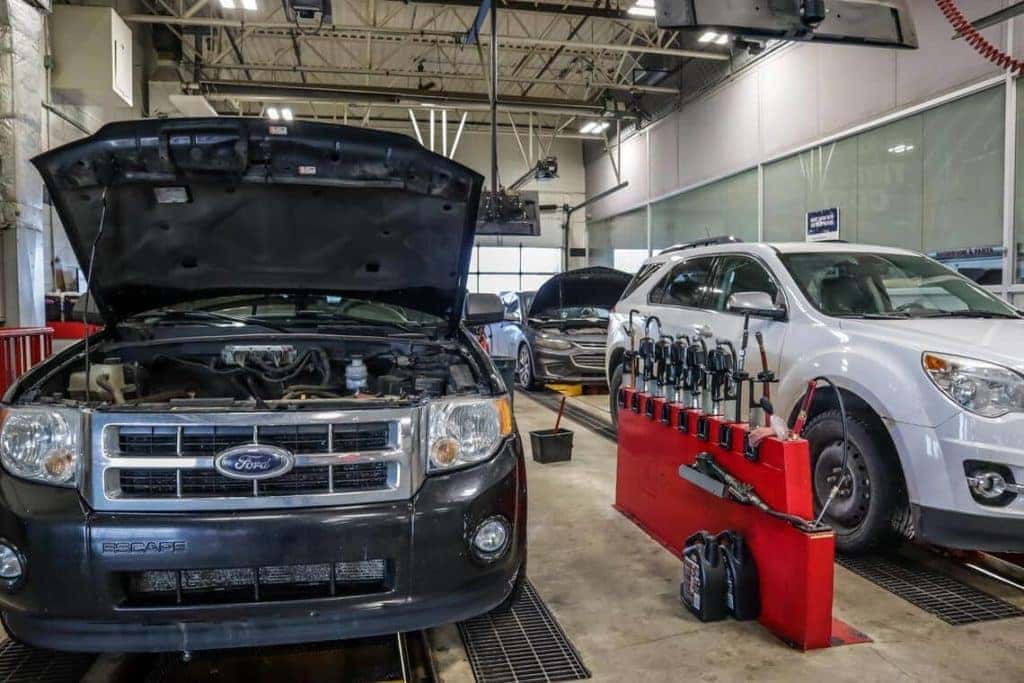 Cars in an auto repair garage, one with an open hood, surrounded by tools and equipment.
