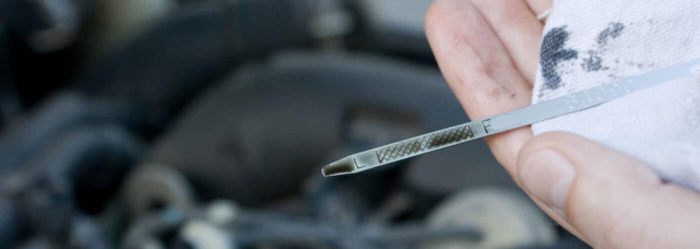 Close-up of a hand holding a car oil dipstick, partially wiped, indicating oil level.