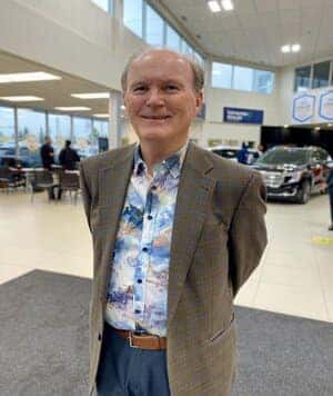 Man in a jacket stands in front of a white car, with a Chevrolet logo and "EV" text overlay.