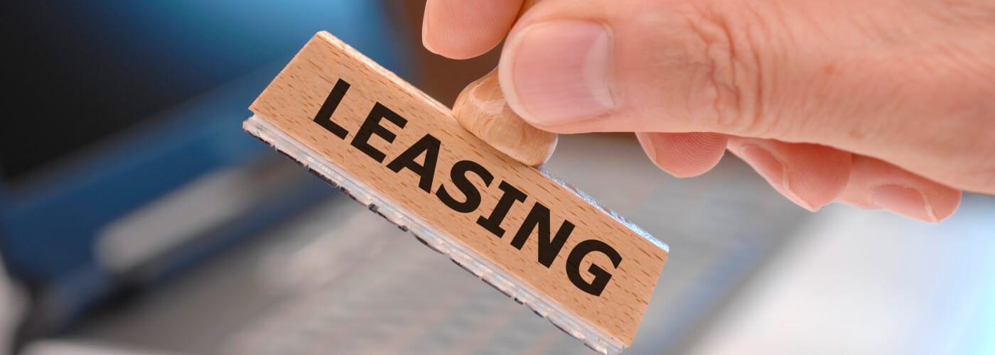 Hand holding a stamp labeled "Leasing" over a blurred background.