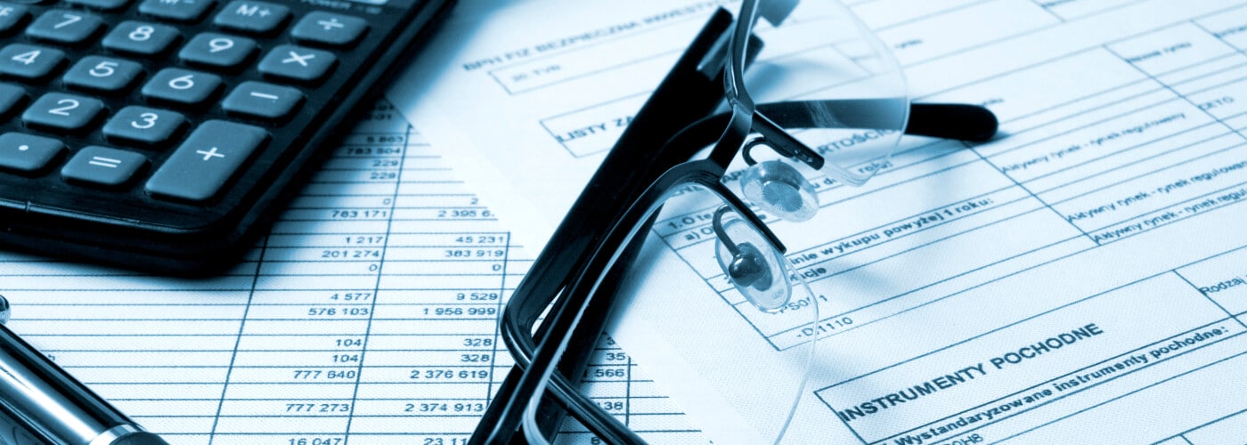 Calculator, glasses, and pen on financial documents with tables and text, suggesting accounting tasks.