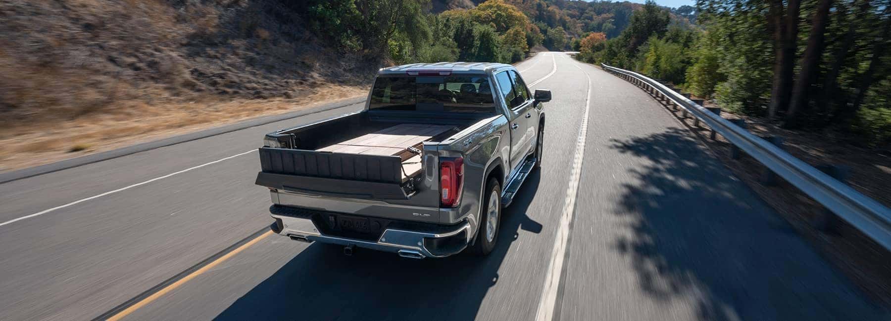 Pickup truck driving on a scenic, tree-lined highway with an open cargo bed.