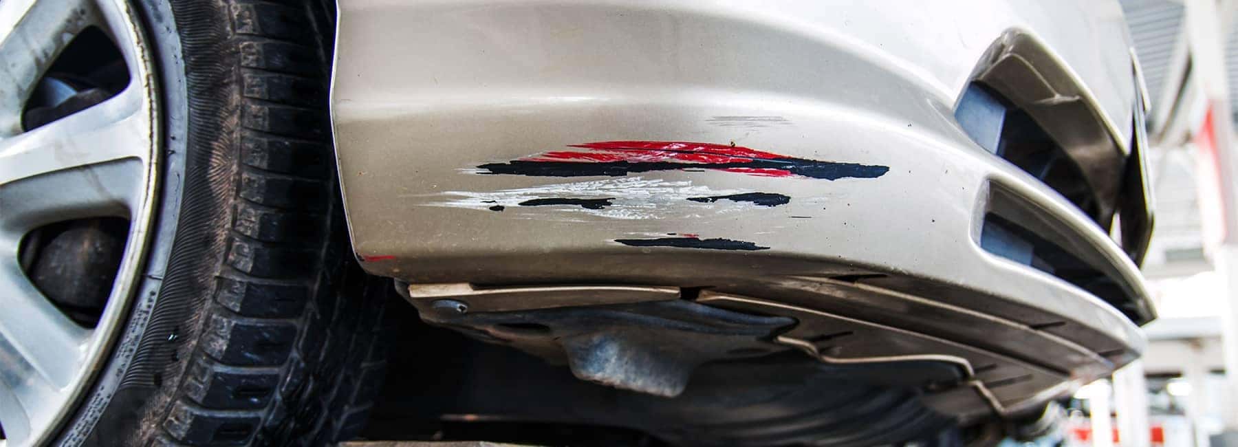 Close-up of a car bumper with visible scratches and scuff marks, indicating damage.