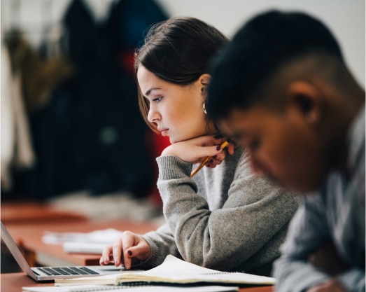 Students focused on studying, one with a laptop and notebook, in a classroom setting.