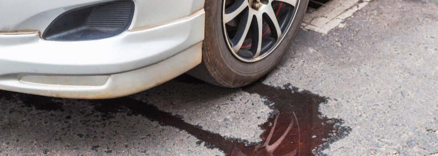 Car parked with a fluid leak on the pavement underneath, near the tire.