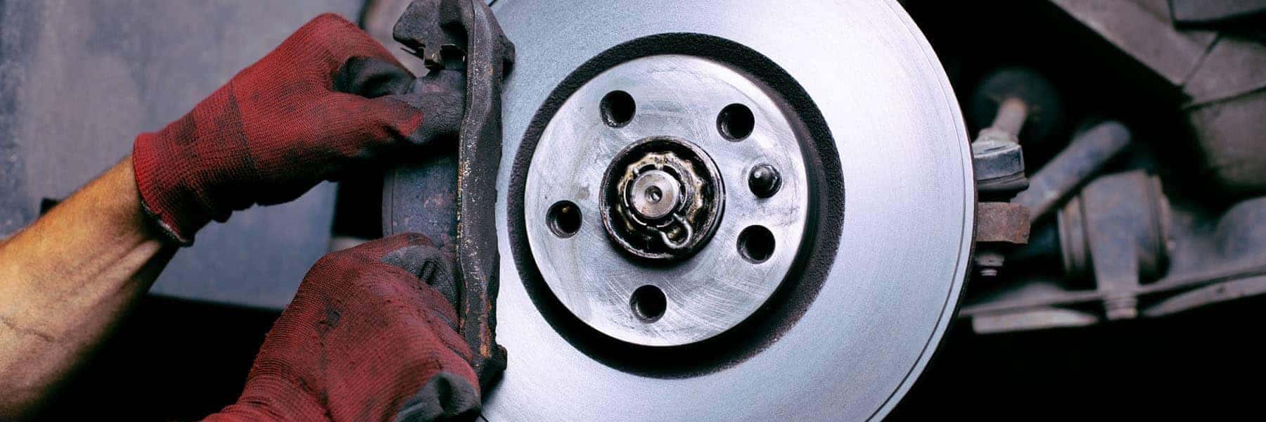 Mechanic with red gloves working on a car brake disc, focusing on repair and maintenance.
