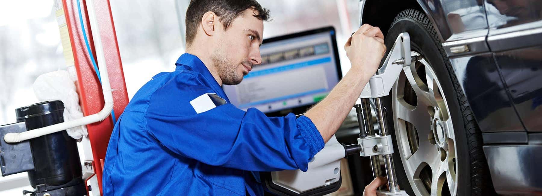 Mechanic in blue uniform aligns car wheel at an auto service center.