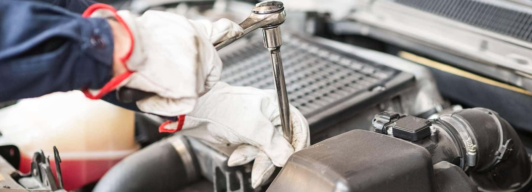 Mechanic using a socket wrench to repair a car engine, emphasizing technical maintenance.