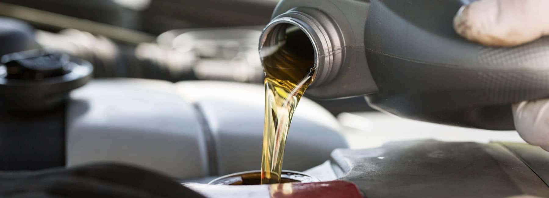 Pouring engine oil into a car engine, close-up of a gloved hand holding the container.