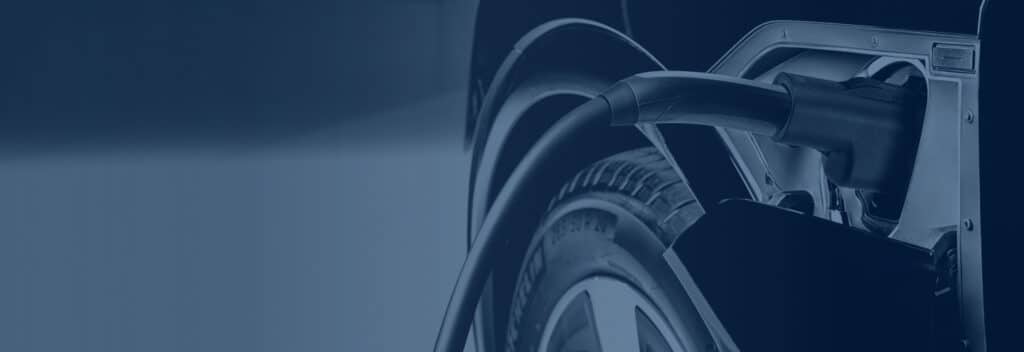 Electric car plugged into a charging station, close-up of a charging cable and vehicle wheel.