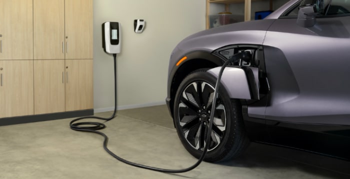 Electric car charging in a garage, plugged into a wall-mounted charger near wooden cabinets.
