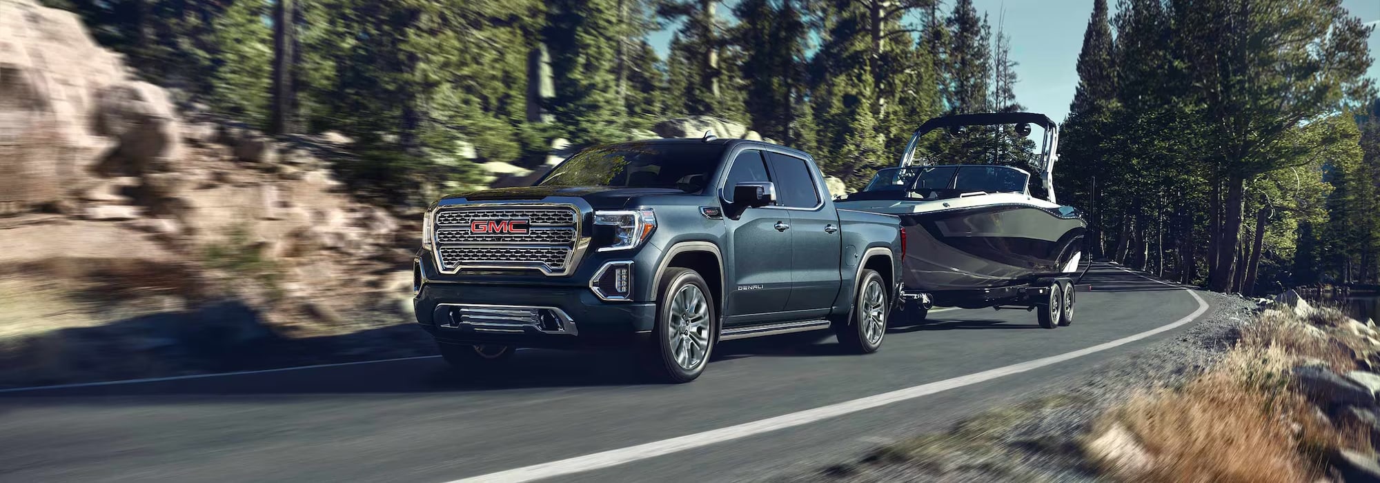 GMC truck towing a boat on a scenic forest road, showcasing its power and utility.