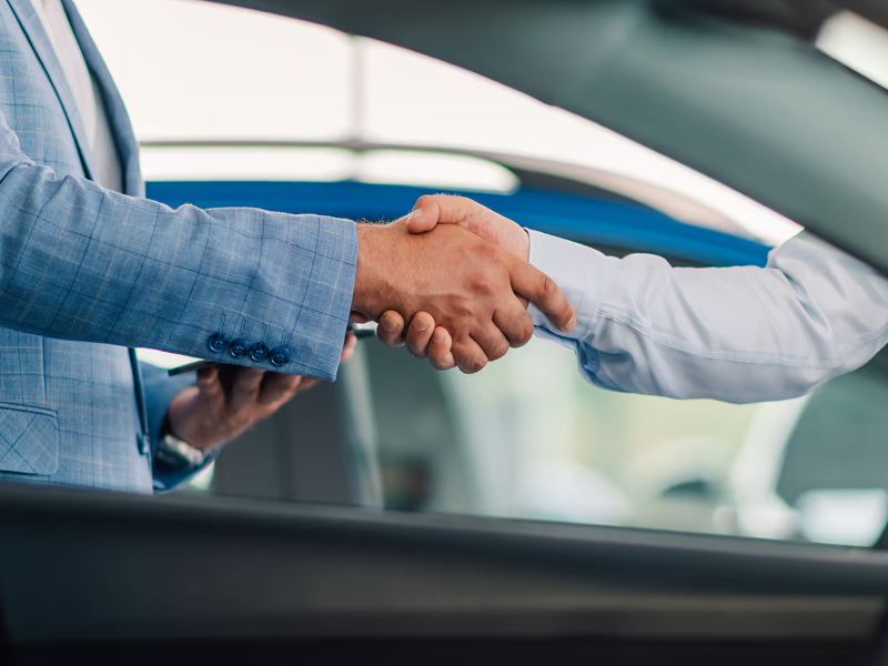 Two people in business suits shaking hands near a car, symbolizing a successful deal.